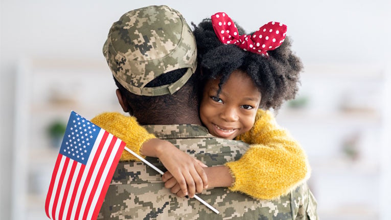 A-va-loan-benefits-those-who-have-served-soldier-getting-hugged-by-his-daughter-holding-a-flag.