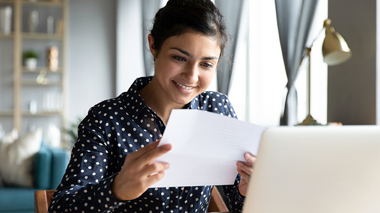 Smiling indian woman holding reading paper letter sit at table