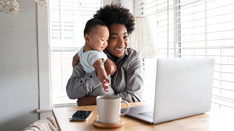Woman applying for a home loan on her laptop while holding her beautul baby.