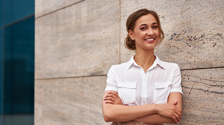 Caucasian middle aged business woman standing arms crossed outdoor, leaning against a building.